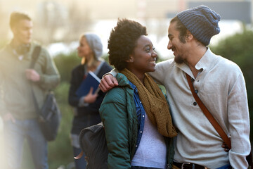 Students, university and conversation of interracial couple of friends on campus with hug and an...
