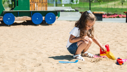 A little girl playing in the sandbox at the playground outdoors. Child playing with sand molds. Outdoor creative activities for kids.