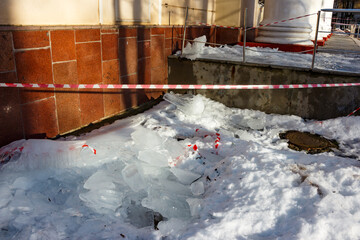 Dangerous place under the roof of a building fenced off with tape with falling icicles and ice in...