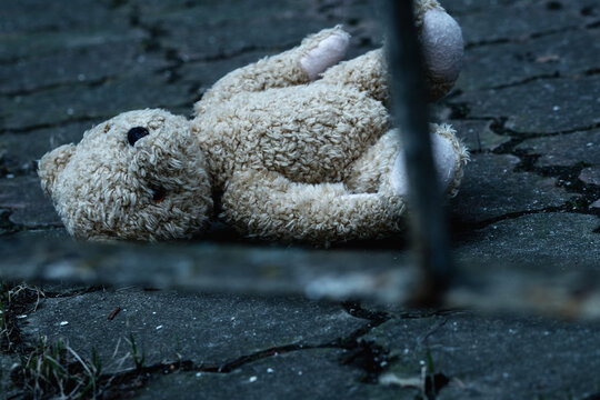 Lost childhood and broken life concept. The teddy bear is lying down on the dirty asphalt Horizontal image.