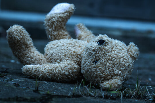 The teddy bear is lying down on the dirty asphalt as symbol of lost childhood, children's loneliness, pain and depression. Horizontal image.