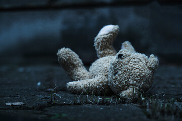Conceptual image: lost childhood, loneliness, pain and depression. Dirty toy Teddy bear lying down outdoors. Close up.