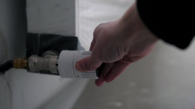 Man adjusts the temperature of the battery radiator at home, heating battery with temperature regulator close-up view