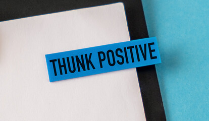 Blue sticky note with THUNK POSITIVE, attached to a composition notebook on blue background.