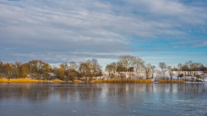 Obraz premium Winter landscape by frozen lake with trees on a snowy shore