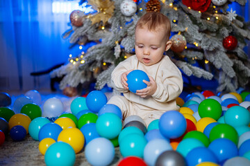 Fototapeta na wymiar Small child plays with colored balls in the room by the Christmas tree