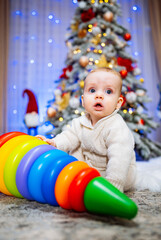 Fototapeta na wymiar Cute baby playing with toy on the floor in front of the Christmas tree