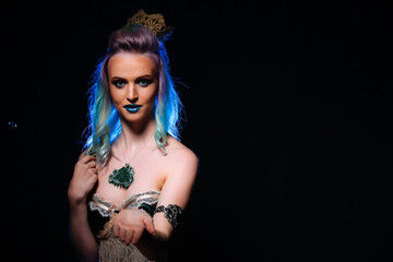 Beautiful young woman with blue hair and crown is posing in the studio on black background.