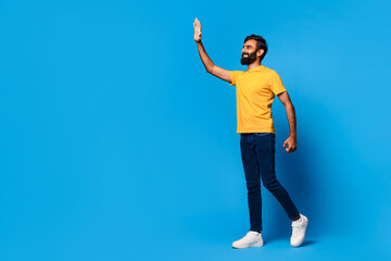 Indian man in yellow waving hello on blue background - obrazy, fototapety, plakaty