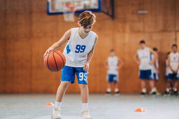 A junior athlete is practicing basketball on training at indoor court.
