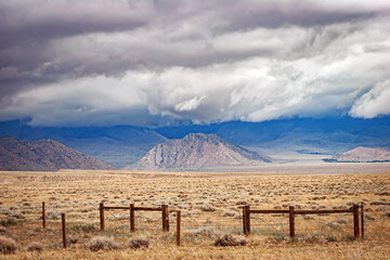 Summer prairie landscape of grasslands, wood fence, hills and cloud covered peaks of a distant...