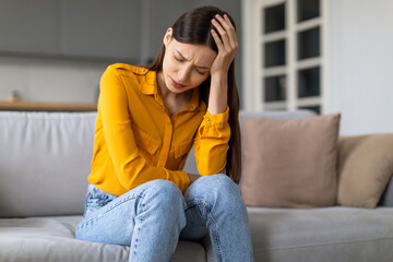 Stressed young woman with headache sitting on the couch