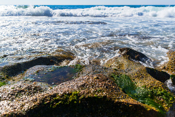 Rock Formation on a Rocky and Sandy Beach Shore With Splashing Blue Sea Waves During a Sunny Summer Day