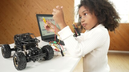 Smart african girl build robotic car while using wires while using laptop setting or writing prompt code. Skilled female student working on computer in STEM technology online classroom. Erudition.