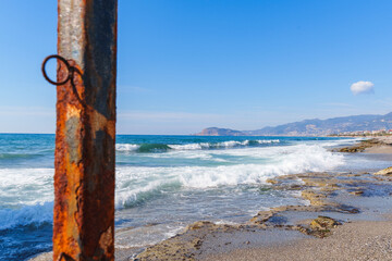 Close Up Shot of a Rusty Iron Steel Pier Bar on a Sandy Beach Infront of the Clear Blue Ocean waves