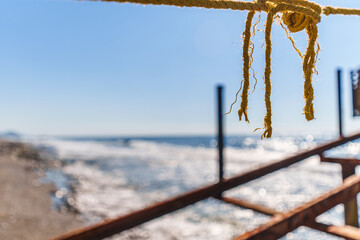 Fototapeta premium Rope String knot Hanging on a Wooden Boardwalk Bay at a Sandy Beach Infront of the Blue Sea and Sky