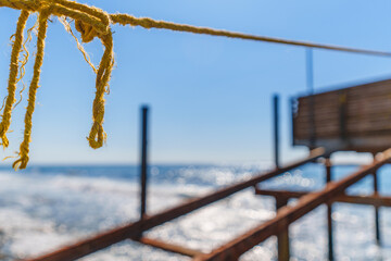 Fototapeta premium Rope String knot Hanging on a Wooden Boardwalk Bay at a Sandy Beach Infront of the Blue Sea and Sky