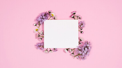 Natural twigs and flowers of lilacs and daisies around a rectangular white piece of paper. Сoming of spring. Pink background.