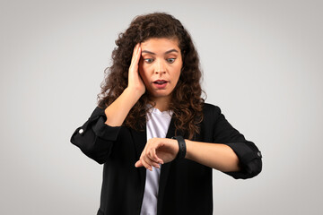 Shocked businesswoman checking time on her smartwatch and touching cheek, time management or...