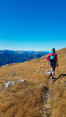 Fototapeta na wymiar Hiker woman on idyllic hiking trail on alpine meadow with scenic view of majestic Hochschwab mountain range, Styria, Austria. Wanderlust in remote Austrian Alps. Sense of escapism, peace, reflection