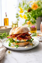 Bacon and egg breakfast sandwich in a white kitchen on the table with a runny yolk - 735398357
