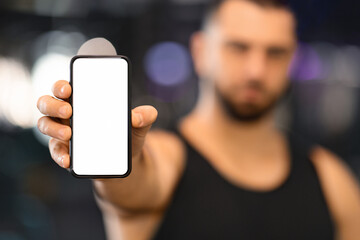 Sports App. Serious muscular man holding blank smartphone in hand