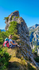Hiker woman resting next to unique rock formation with panoramic view of majestic Hochschwab massif, Styria, Austria. Idyllic hiking trail in remote Austrian Alps. Sense of escapism, peace, reflection