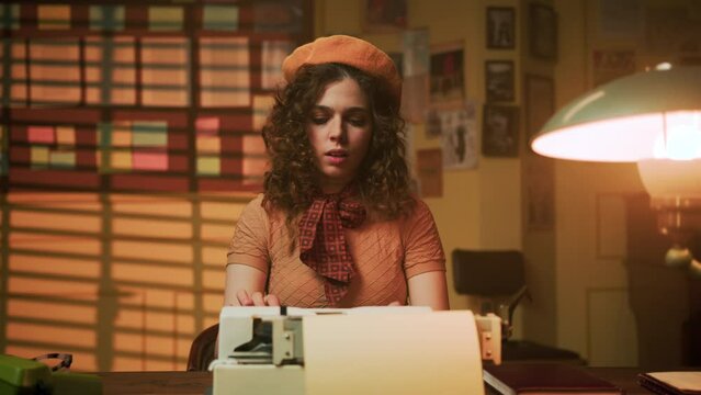 young woman with curly hair in beret, dressed in retro style typing editorial article on typewriter. She embodies the image of journalist at work in vintage office setting