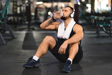 Fototapeta na wymiar Sporty young man drinking water from bottle after workout at modern gym