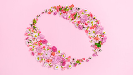 Heads of natural fresh flowers form an oval frame. Pink background.