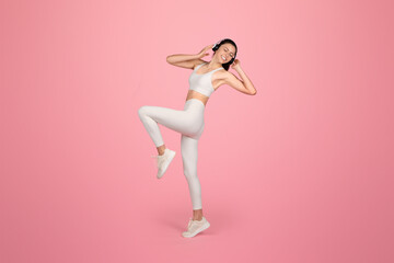 Energetic and joyful woman in white sportswear with headphones dancing or doing a fitness dance