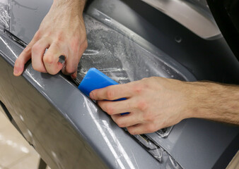 Close up of paint protection film installation on front bumper of modern luxury car. PPF is polyurethane film applied to car surface to protect the paint from stone chips, bug splatter, and abrasion. 