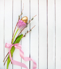 Pink tulips, willow branches and a golden egg on a white wooden table. Easter card.