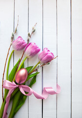 Pink tulips, willow branches and a golden egg on a white wooden table. Easter card.