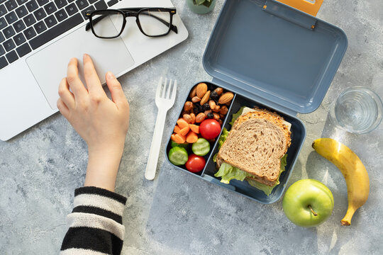 Healthy business lunch at workplace. Sandwich, vegetables, fruid and water lunch box on working desk with laptop, glasses.