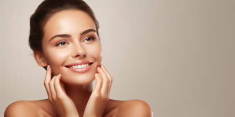 Radiant young brunette woman smiling, touching face, on beige backdrop. Concept of skincare beauty, beauty, joyful demeanor, and positive attitude. Wide banner with copy space - obrazy, fototapety, plakaty