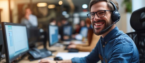 Fototapeta premium Happy young man with headphones and smiling while working on desktop computer in modern office