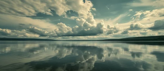 Fototapeten Tranquil lake landscape with reflective water surface under moody overcast sky © AkuAku