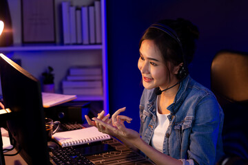 Host channel Asian influencer talking in broadcast streaming online wearing headsets on social media with pc recording, greeting listeners and coaching market online at neon modern studio. Stratagem.
