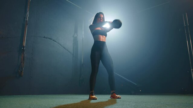 In a gym bathed in dramatic backlighting, a dedicated female athlete performs a series of kettlebell swings, her silhouette casting a striking figure against the intense glow. Camera 8K RAW. 