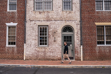 Stylish Man Walking Down a Street in Front of a Dual Colored Brick Facade in Historic Williamsburg Virginia