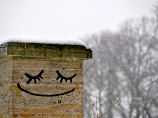 stone column in a park with asmiley face painted on it during snowing winter weather
