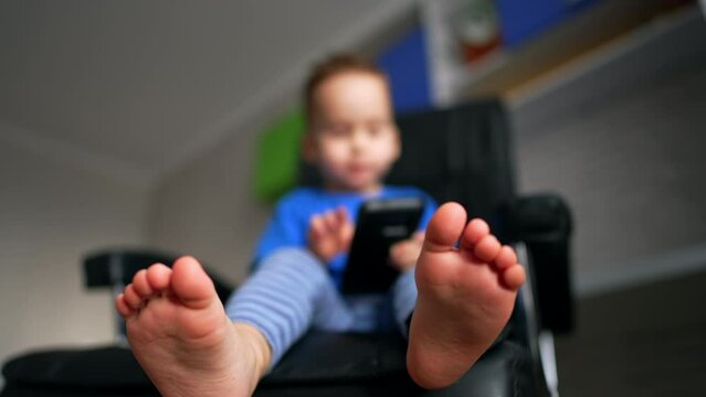Toddler's bare feet close up. Low angle view on the baby boy with smartphone in hands. Blurred backdrop.