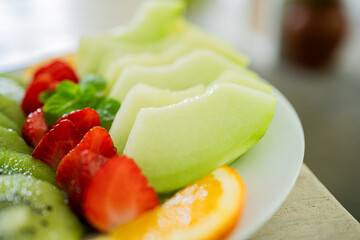 mixed fruit plate containing melon, strawberries, oranges and kiwi. The main focus is on melons.