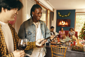 Smiling male friends drinking wine while looking on mobile phone during festive home party