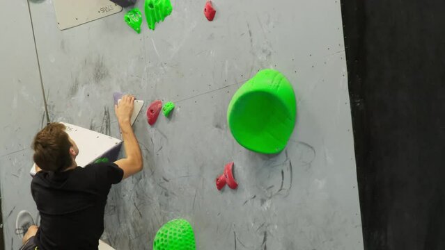 Man ascends climbing wall with resolve and assurance. Sportsman maintains unflinching focus maneuvering on holds and grips