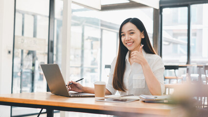 Business technology concept, Cheerful young woman giving a thumbs up while working on her laptop at a bright and airy cafe table.