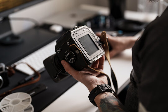 An adult man is engrossed in adjusting the settings on a medium format camera, highlighting meticulous attention to detail in a professional studio