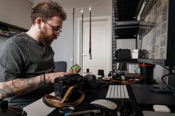 An adult man is deeply focused on his photography equipment at a well-organized workspace,...
