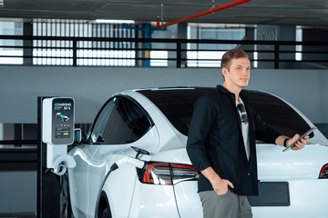 Young man travel with EV electric car to shopping center parking lot charging in downtown city...